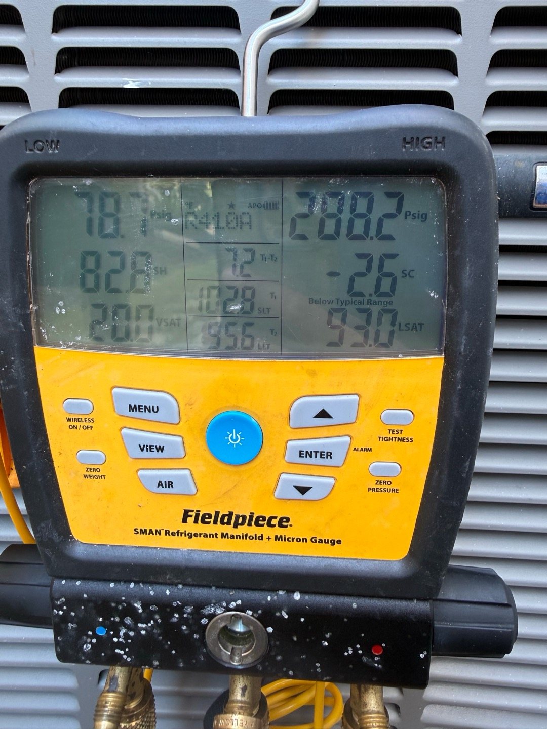 Digital refrigerant manifold gauges on an outdoor AC unit reading system pressures, superheat, and subcooling