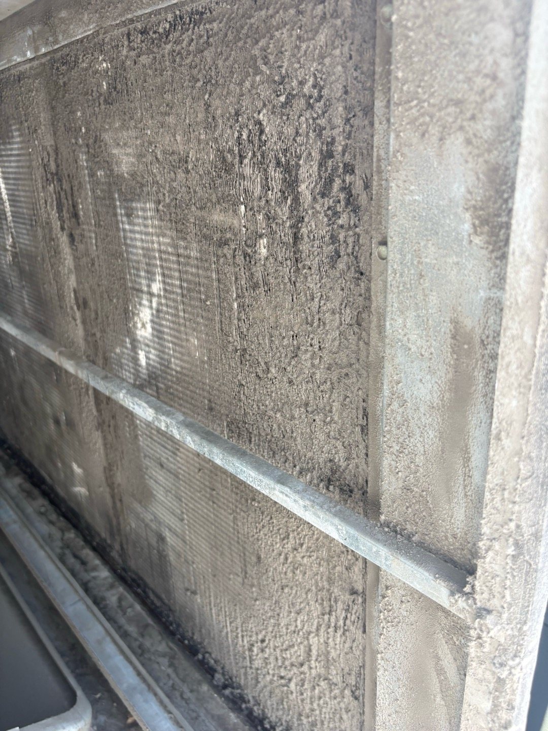A dust-covered indoor cooling coil face, the kind of buildup that starts when air bypasses or pushes through a worn-out filter