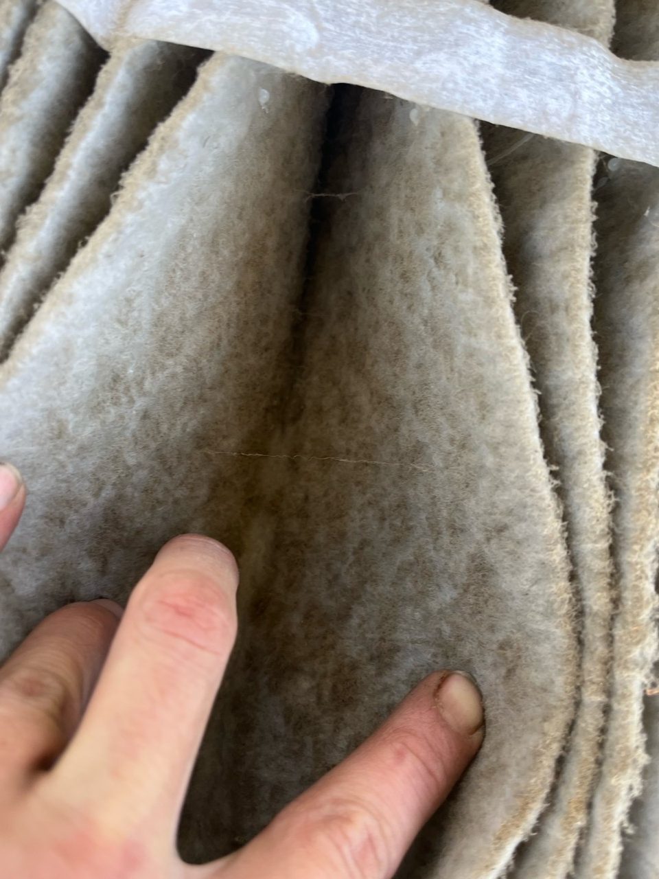 Fingers pulling apart the pleats of a dirty air filter to show dust packed deep inside