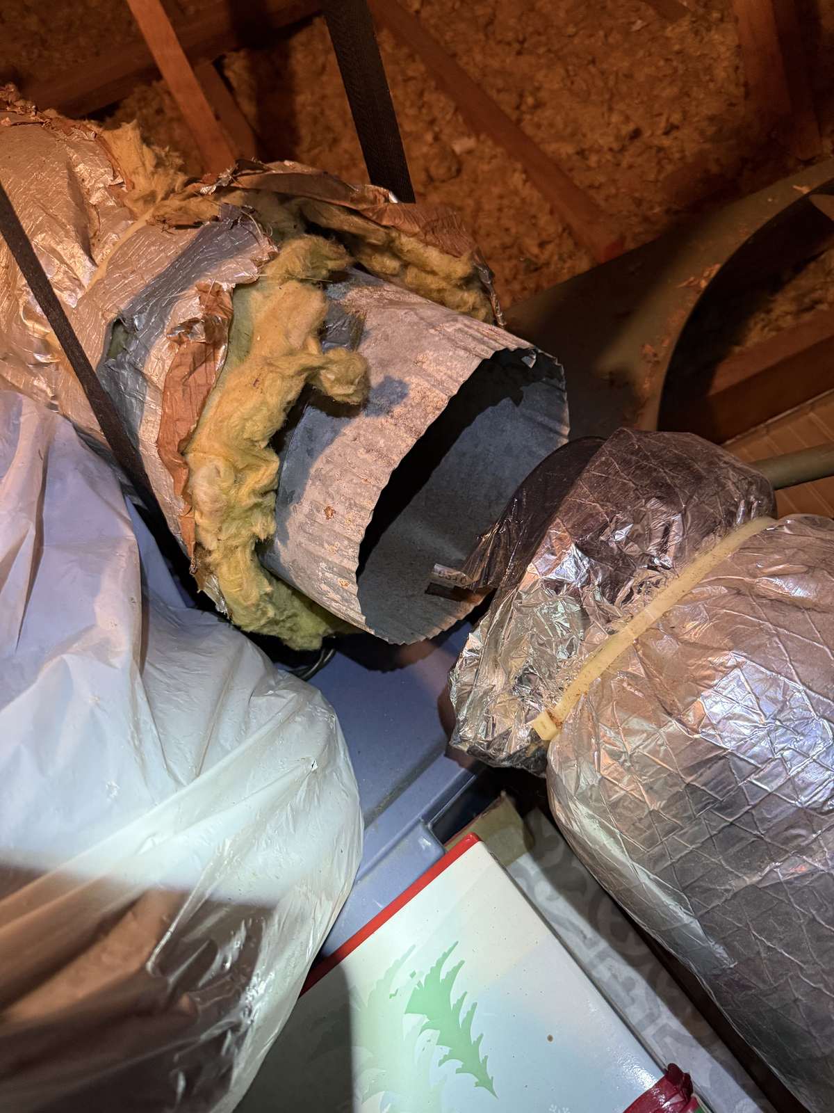 Flexible attic duct with torn foil and insulation, pulled apart from the next section with a gap between the two ends