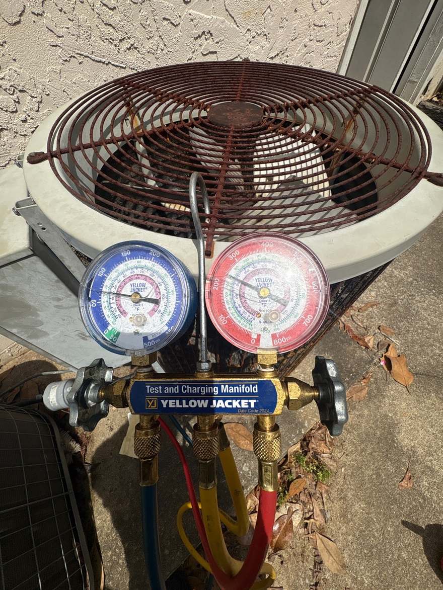 Refrigerant manifold gauges hanging on a residential outdoor AC unit during a cooling diagnostic