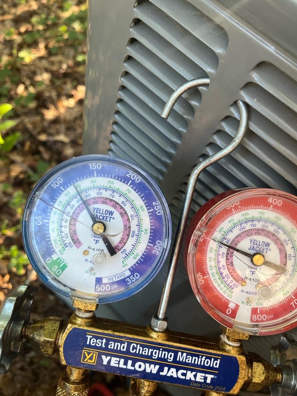Close-up of blue and red refrigerant manifold gauges hooked onto an outdoor air conditioner, showing system pressures
