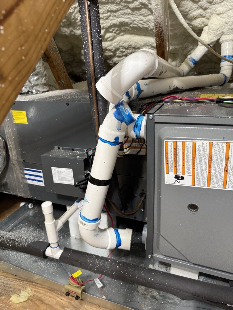 High-efficiency condensing gas furnace in an attic with white PVC vent, intake and condensate drain pipes