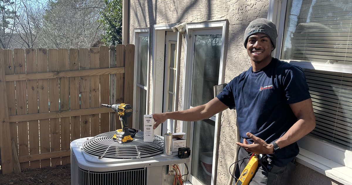 John Davis Heating and Air technician smiling beside an outdoor AC unit during a tune-up with gauges connected