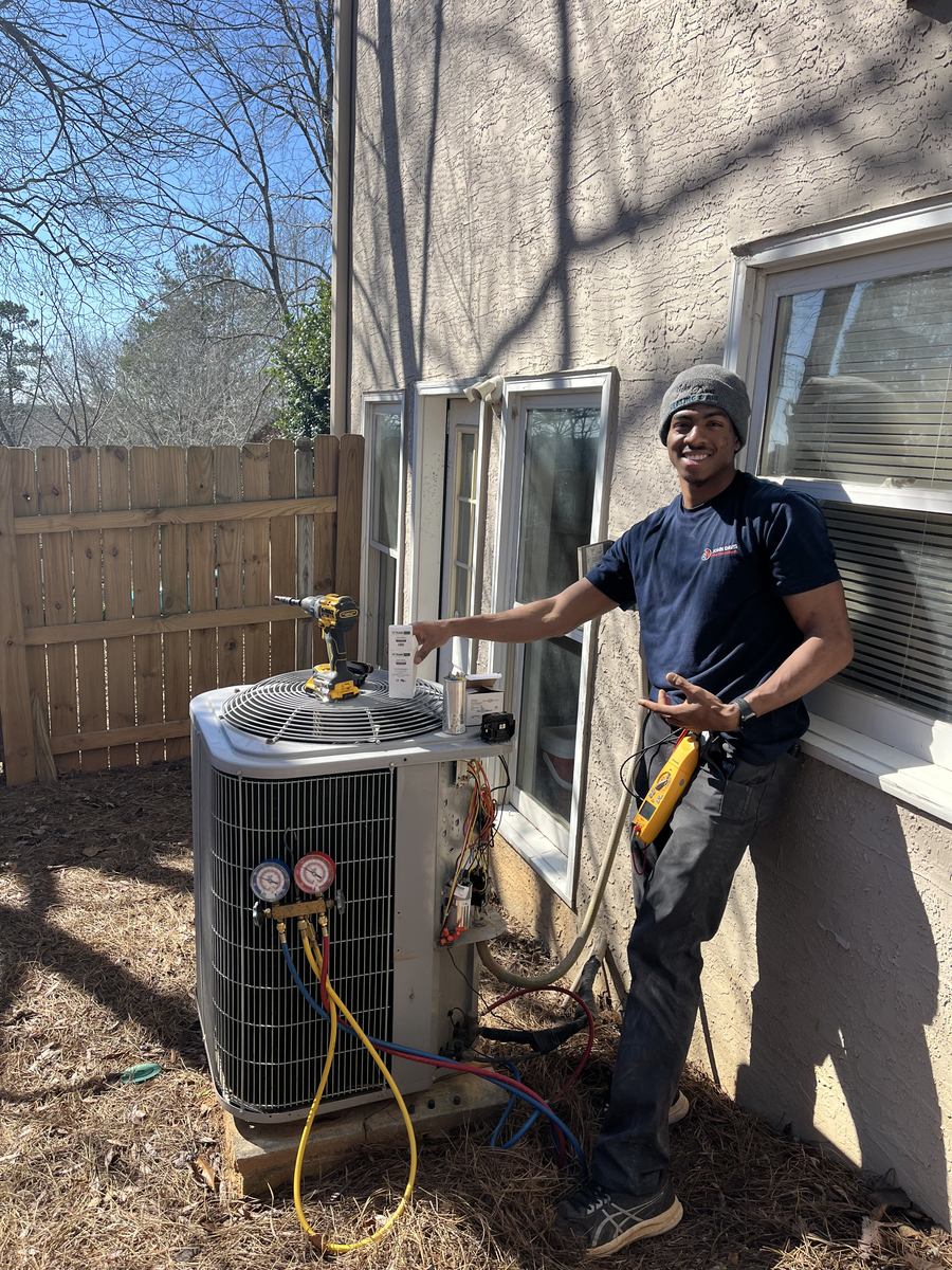 John Davis Heating and Air technician smiling beside an outdoor AC unit during a tune-up with gauges connected