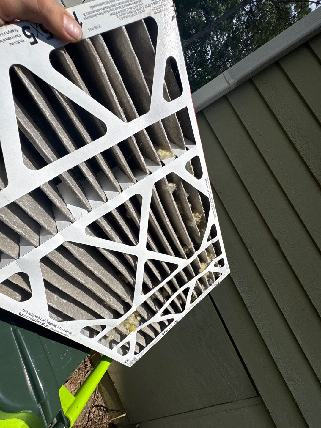 A loaded pleated air filter held up outdoors during a tune-up, with dust and debris packed into the pleats