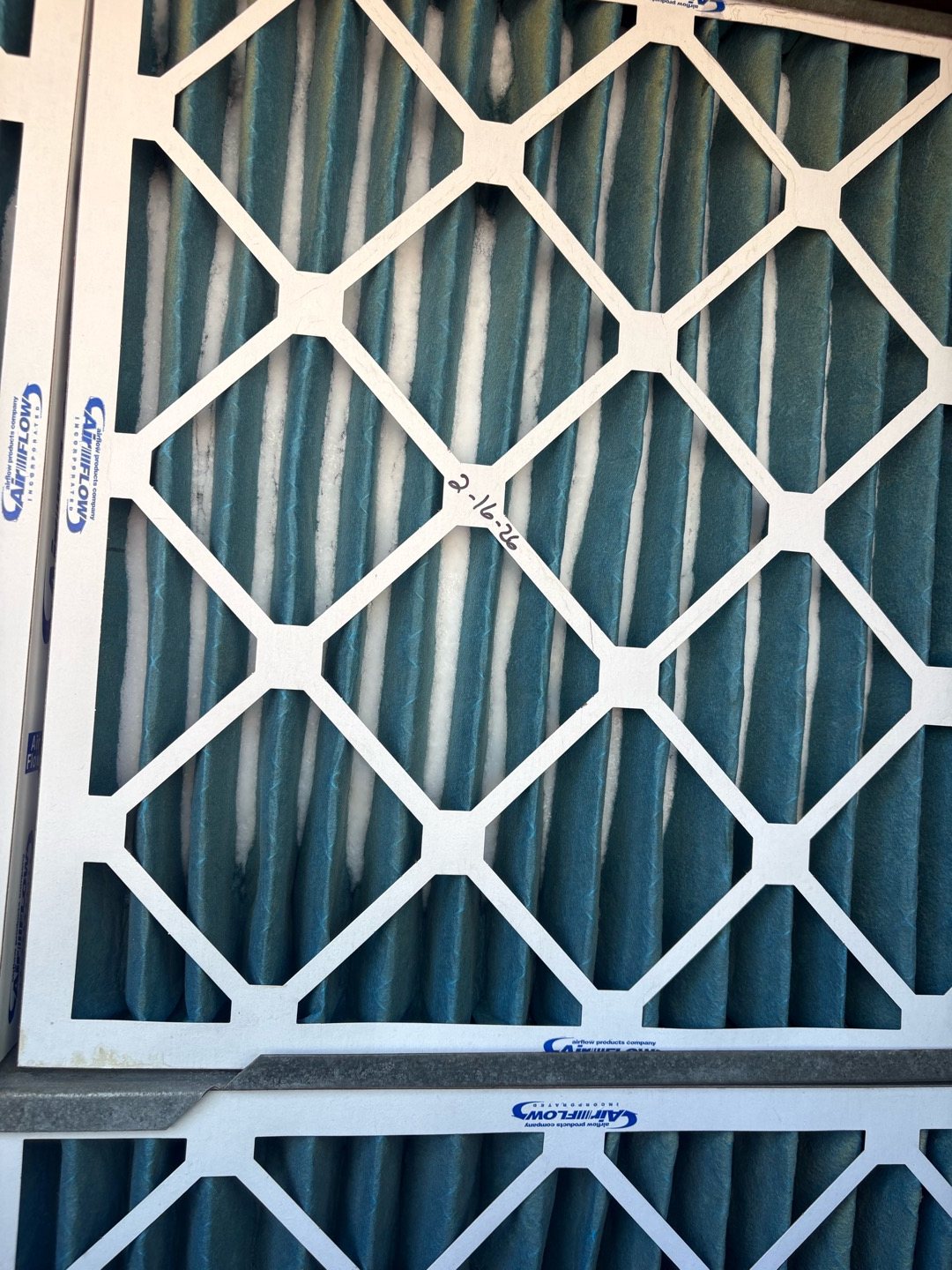 A new, clean pleated air filter with white pleats and a cardboard frame, ready to go into a filter slot