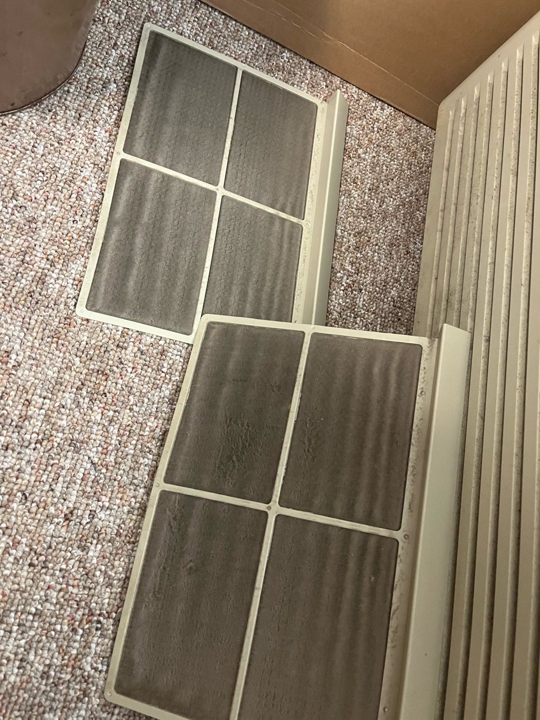 Two hinged return air filter grilles taken down for a filter change, with dust lines on the louvers