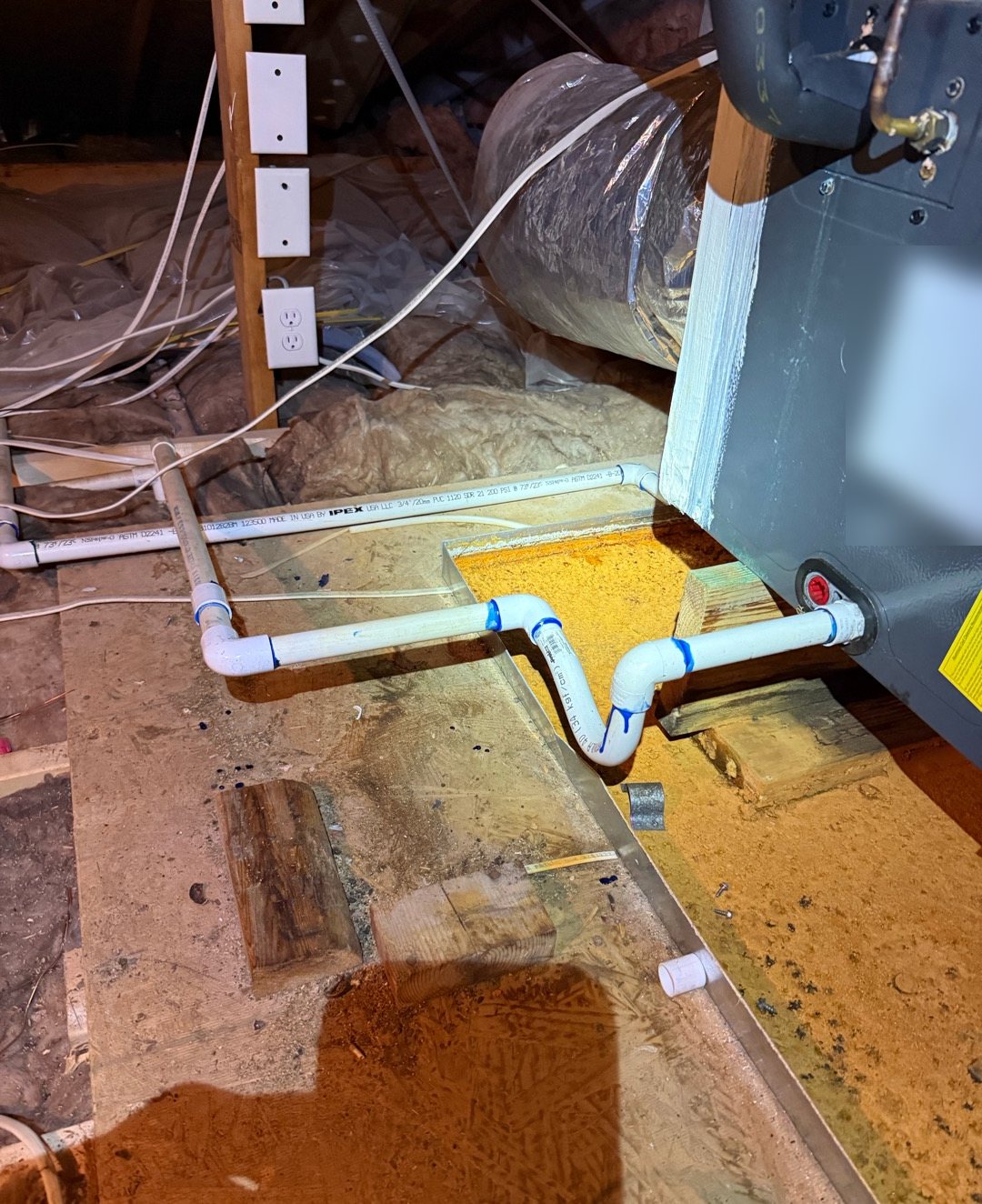 Rust-stained drain pan under an attic air handler with a re-piped white PVC condensate drain line and P-trap