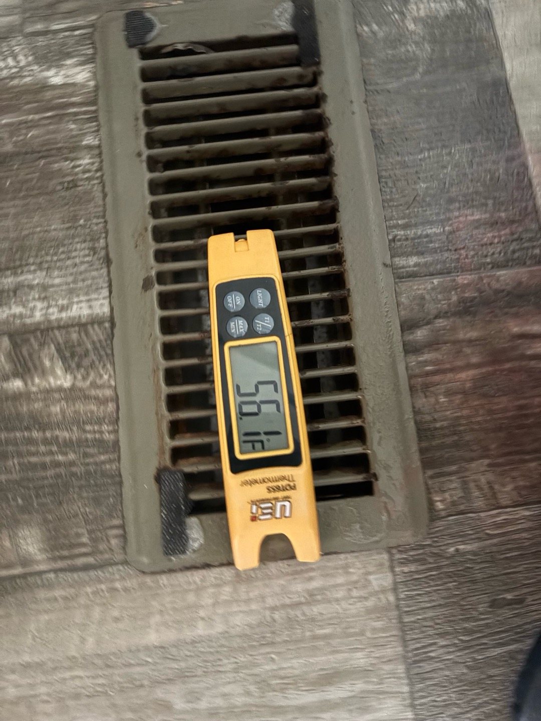 Digital thermometer resting on a floor supply vent to measure the air temperature coming from the AC