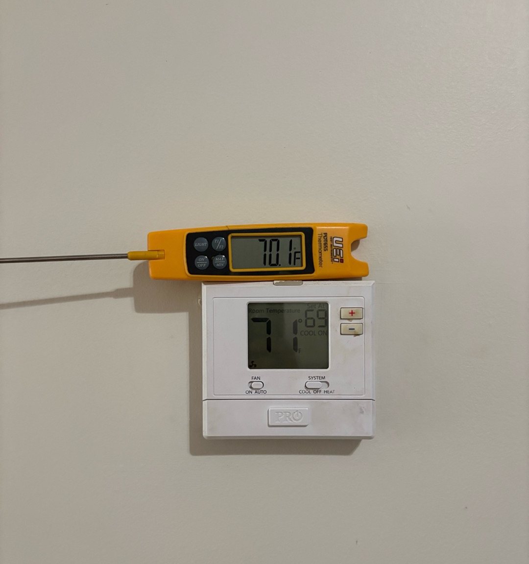 Digital thermometer held beside a wall thermostat to check that the thermostat is reading the room temperature correctly