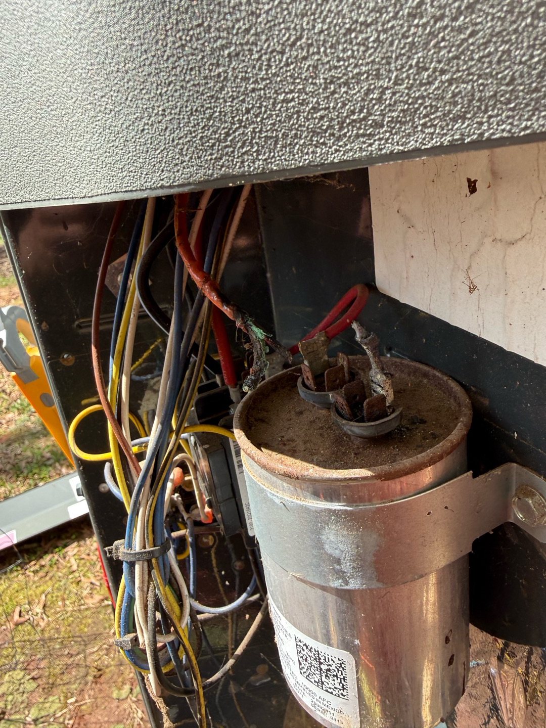 Rusty, worn run capacitor with corroded terminals inside an outdoor AC unit's electrical compartment